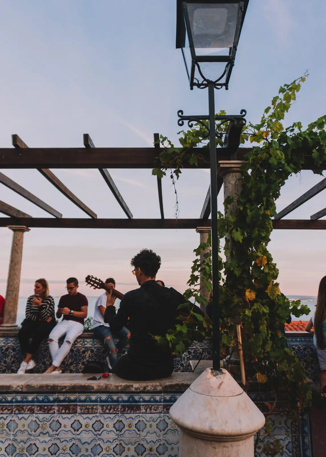 Tra i quartieri di Lisbona: Mirador de Santa Luzia, pergolato in ceramica con ragazzo che suona la chitarra al tramonto
